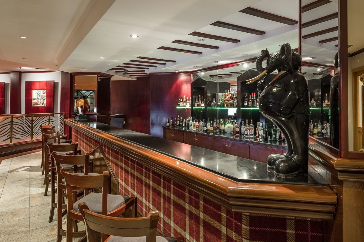 A bar area with a long counter, wooden chairs, and a statue of an elephant.
