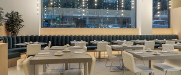 Un restaurante con cabinas y mesas, un amplio ventanal con vista a la calle y luces colgantes.