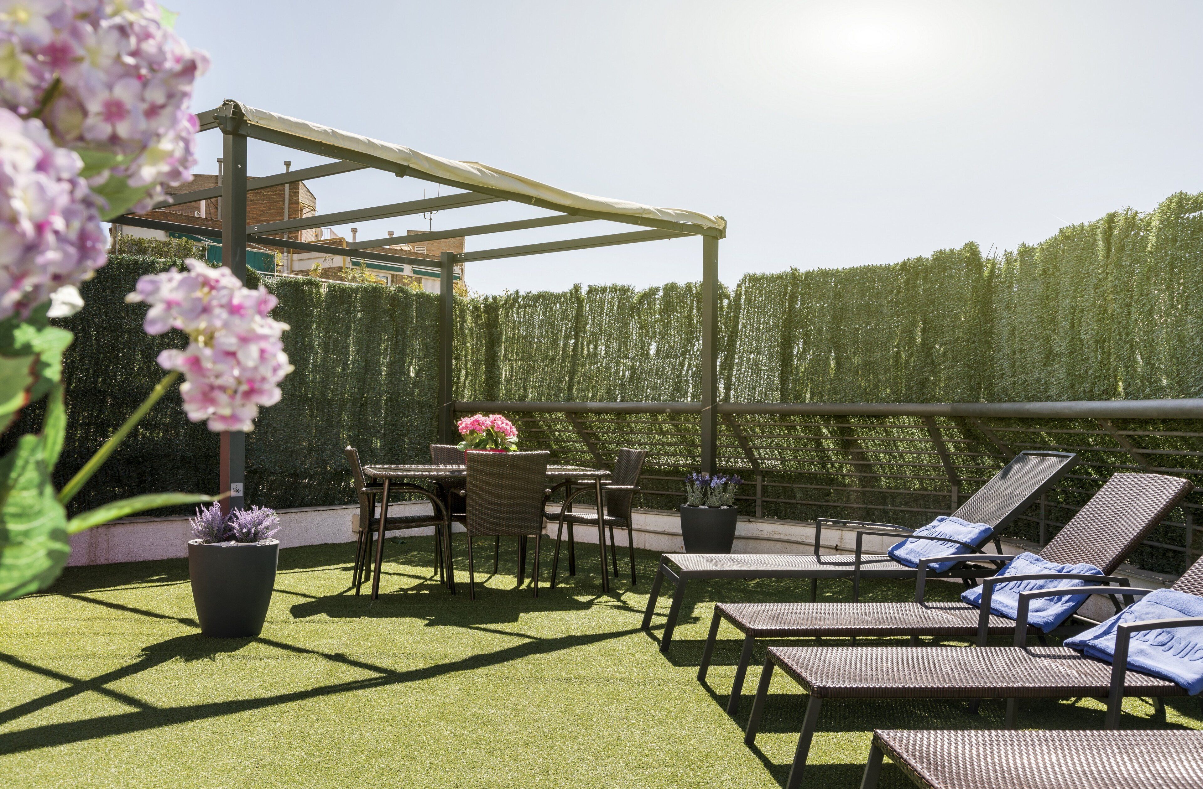 Un patio al aire libre con césped artificial, una pérgola, sillones de descanso y una mesa con sillas.