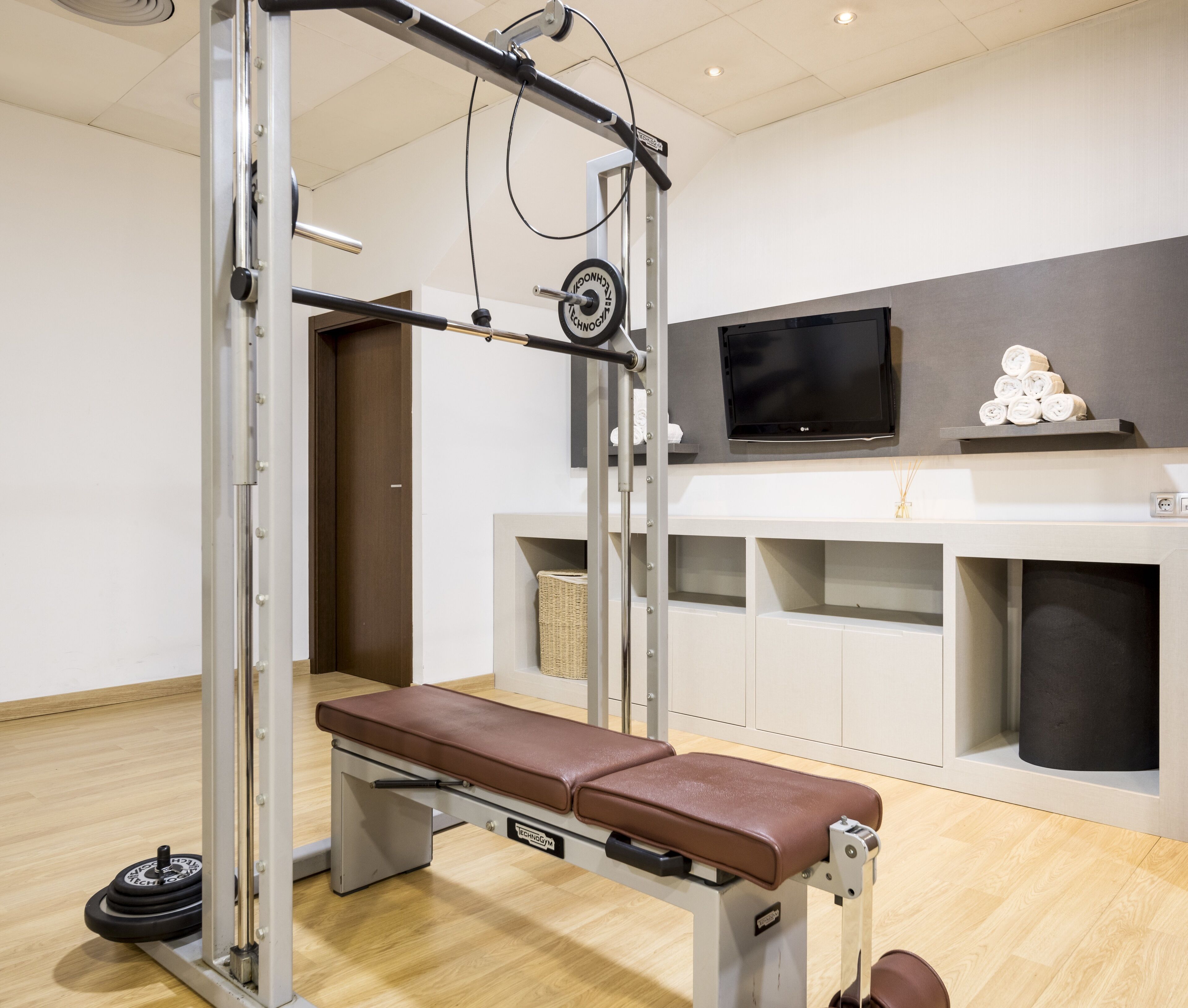 A gym with a bench, weight plates, and a TV on a shelf.