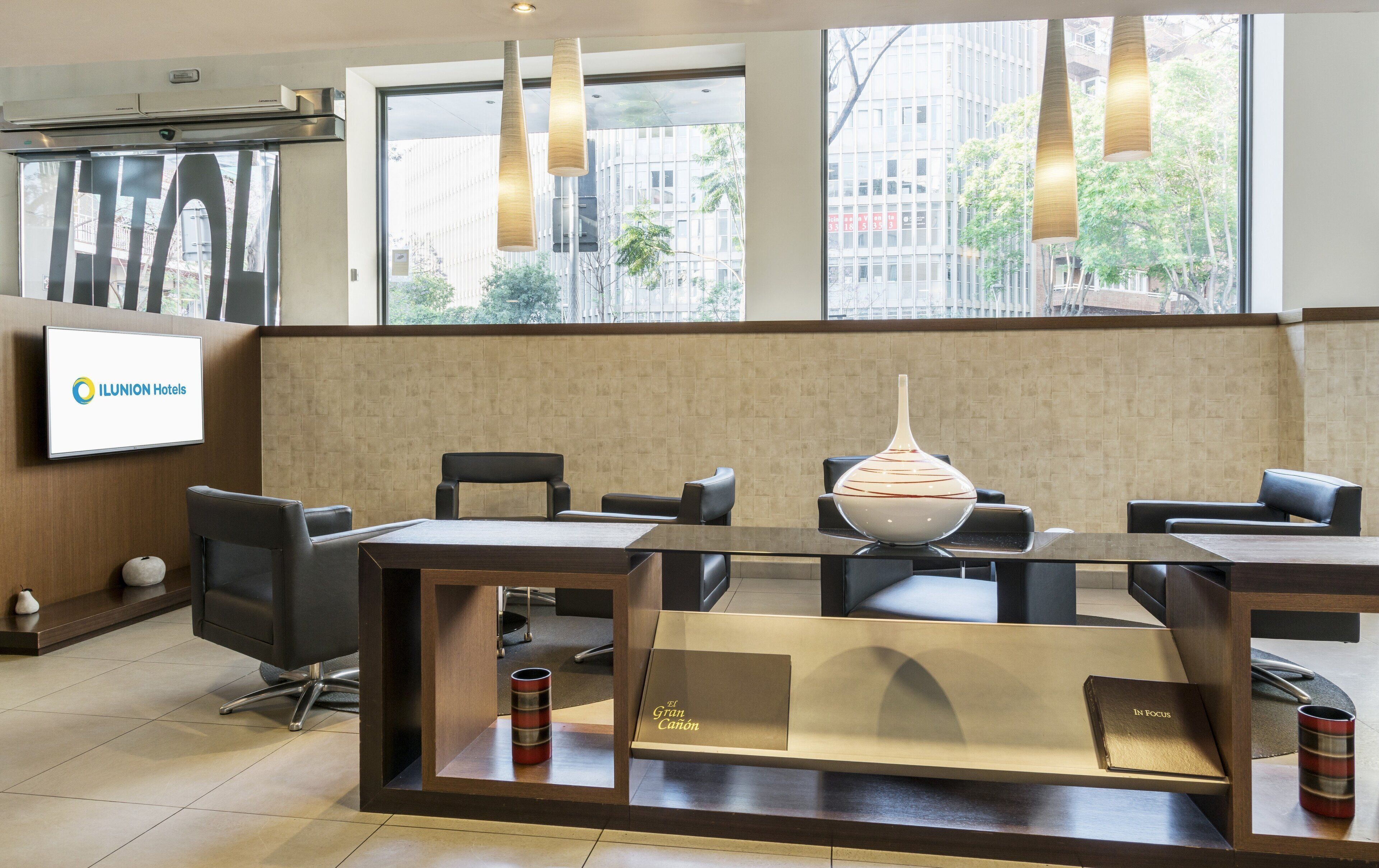 Un hall d’hôtel moderne doté d’un comptoir d’accueil, d’un espace salon et de grandes fenêtres offrant une vue sur la ville.