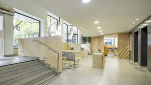 A modern hotel lobby with a staircase, seating area, and large windows. - Hotel ILUNION Auditori (Barcelona)
