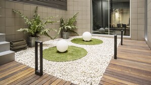 A modern indoor courtyard with a wooden deck, white pebbles, and two spherical planters. - Hotel ILUNION Auditori (Barcelona)