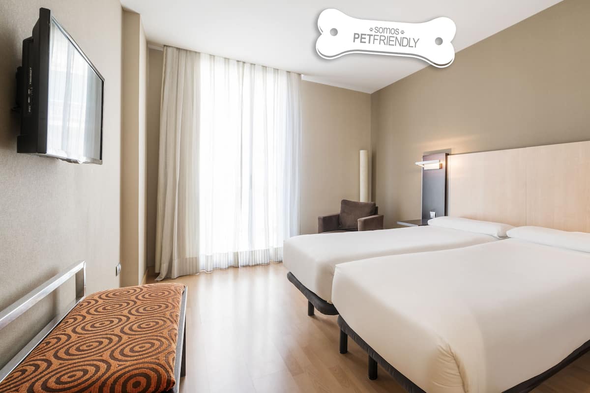 A hotel room with two beds, a TV, a desk, and a sign indicating pet friendliness.