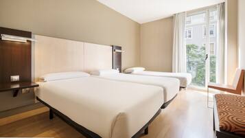 Habitación de hotel con dos camas, un escritorio y una ventana que ofrece vistas a edificios.
