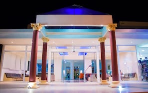 A hotel entrance with a glass door, red columns, and a blue-lit canopy. - Marathon (Rhodes)