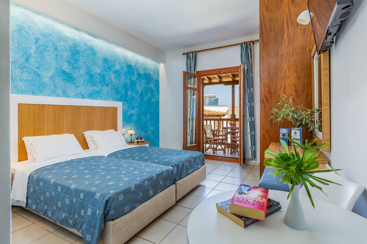 A bedroom with a bed, a nightstand, a potted plant, and a table with books.
