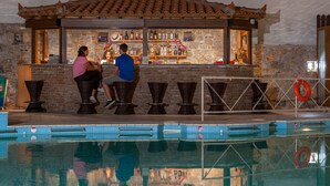 A poolside bar with a stone wall backdrop, wicker chairs, and a lifebuoy. - Aeolos Hotel (Skopelos)