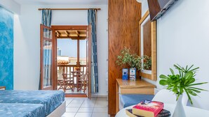 A room with a bed, a desk with books, a plant, and a view through an open door to an outdoor area. - Aeolos Hotel (Skopelos)