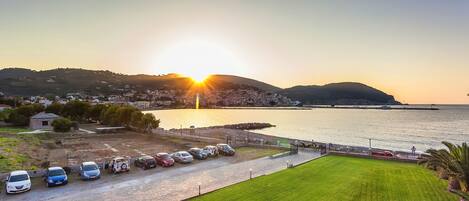 A parking lot with several cars, a grassy area, and a view of the sea at sunset.