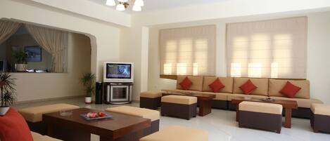 Una sala de estar moderna con un sofá, otomanas, una mesa de centro y una televisión.