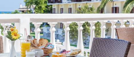 A breakfast tray with various foods and drinks on a balcony overlooking a building with balconies and palm trees.