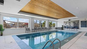 A swimming pool with a wooden ceiling, large windows, and outdoor seating. - Sandman Hotels & Suites Calgary West (Calgary)