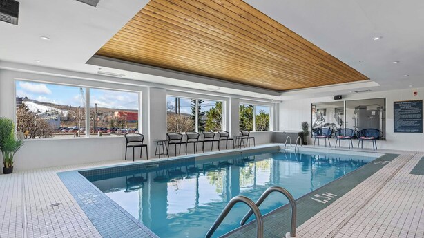 A swimming pool with a wooden ceiling, large windows, and outdoor seating. - Sandman Hotels & Suites Calgary West (Calgary)