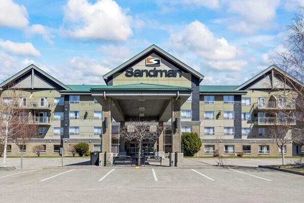 A Sandman hotel with a prominent entrance, a parking lot, and a clear sky. - Sandman Hotels & Suites Calgary West (Calgary)
