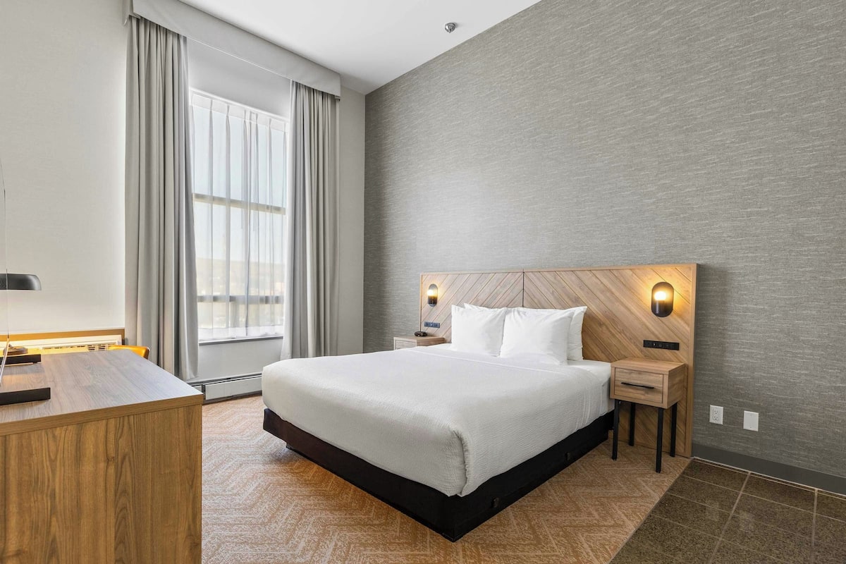 A hotel room with a large bed, wooden headboard, bedside tables, a desk, and a window with curtains.