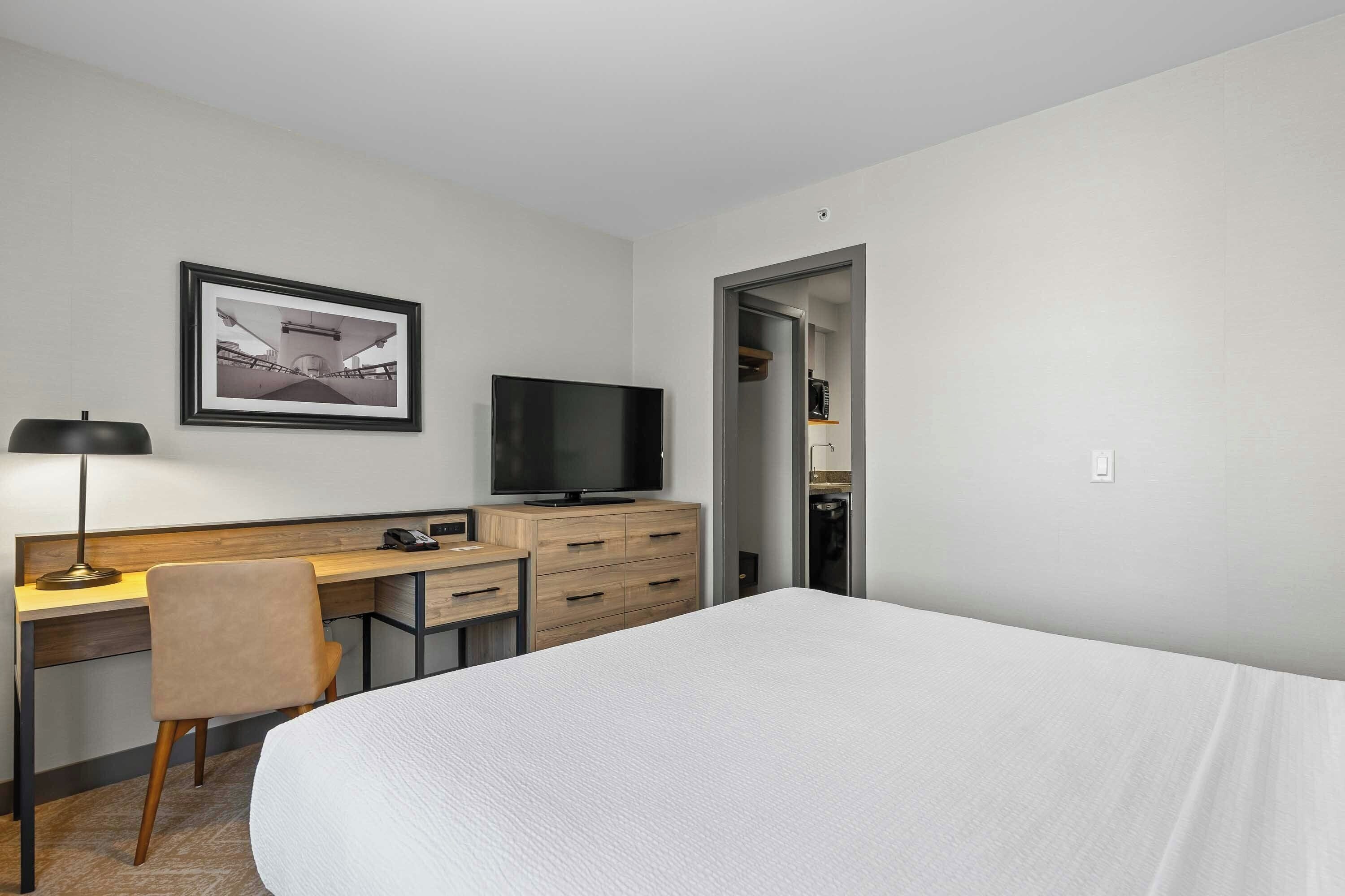 Habitación de hotel con cama, escritorio, silla, televisor y un cuadro en la pared.