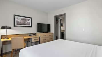 Habitación de hotel con cama, escritorio, silla, televisor y un cuadro en la pared.