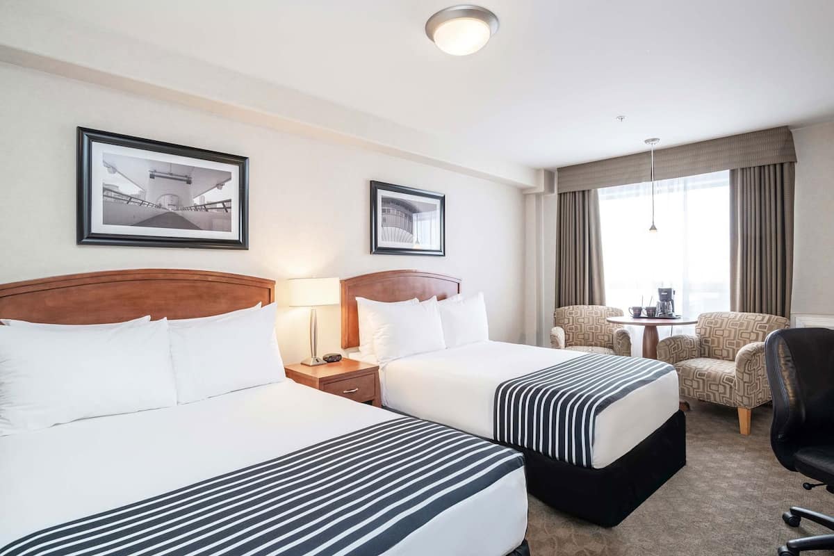 A hotel room with two beds, a desk, a chair, and a window with curtains.