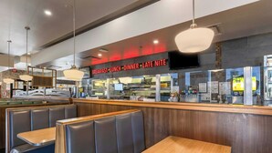 A restaurant interior with booths and tables, a counter with a menu display, and an exit sign. - Sandman Hotels & Suites Calgary West (Calgary)