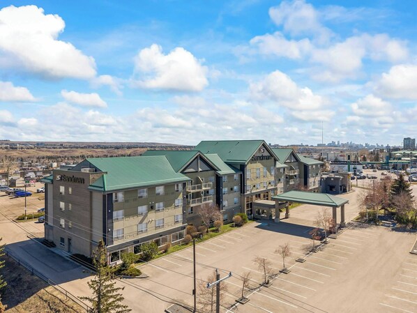 A hotel with multiple buildings, a parking lot, and a cityscape in the background. - Sandman Hotels & Suites Calgary West (Calgary)