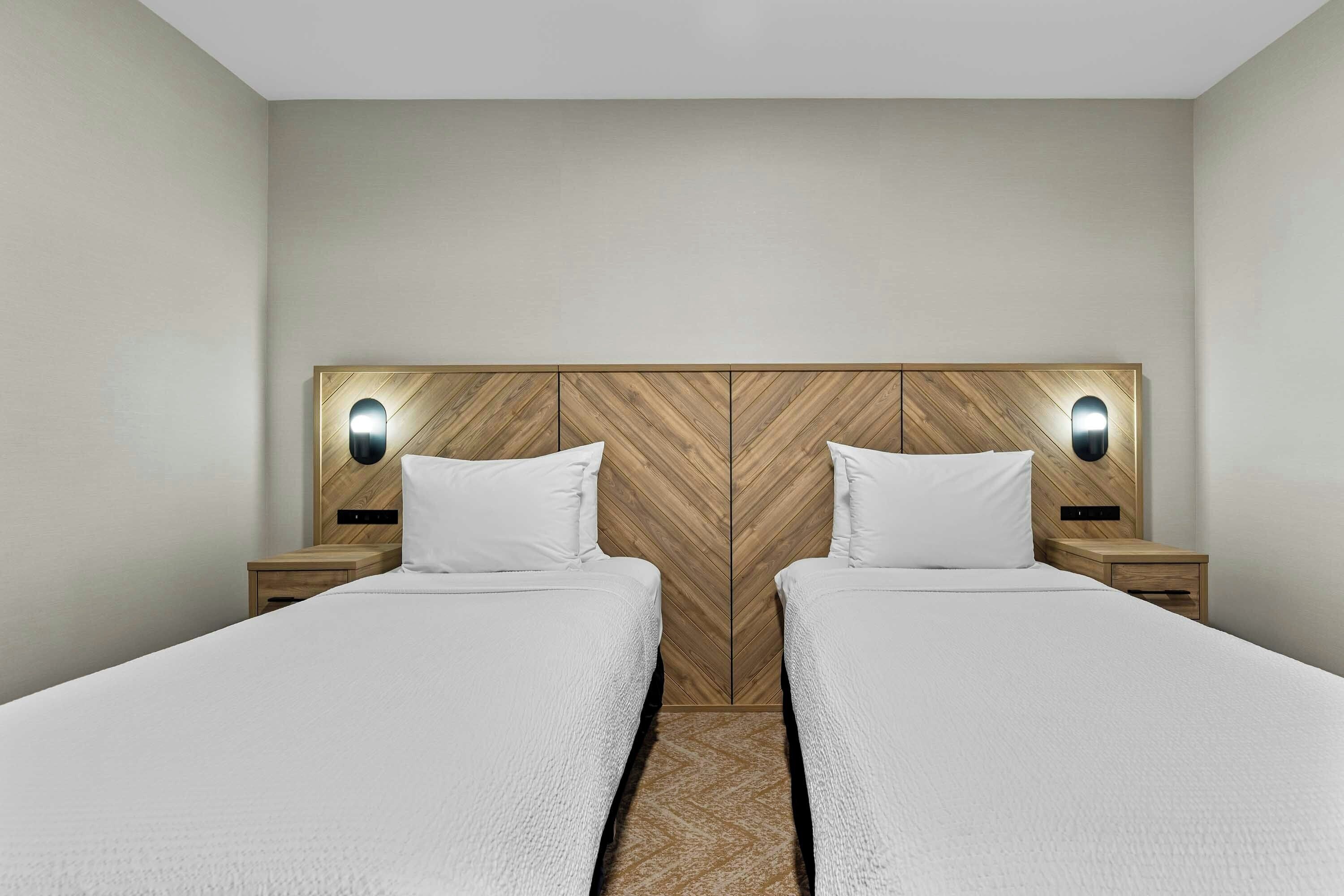 A double room with two beds, wooden headboard, bedside tables, and wall-mounted lights.