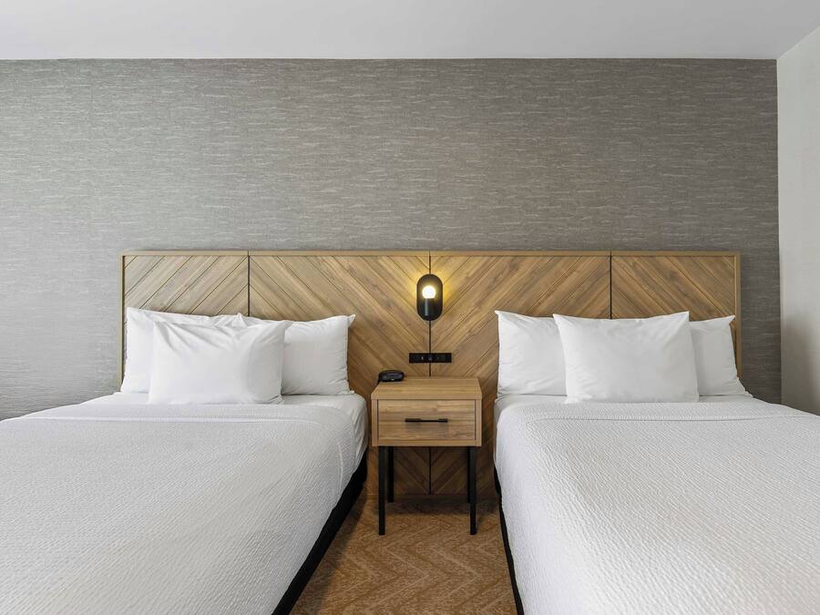 Una habitación de hotel con dos camas, una mesita de noche con lámpara y un cabecero de madera.