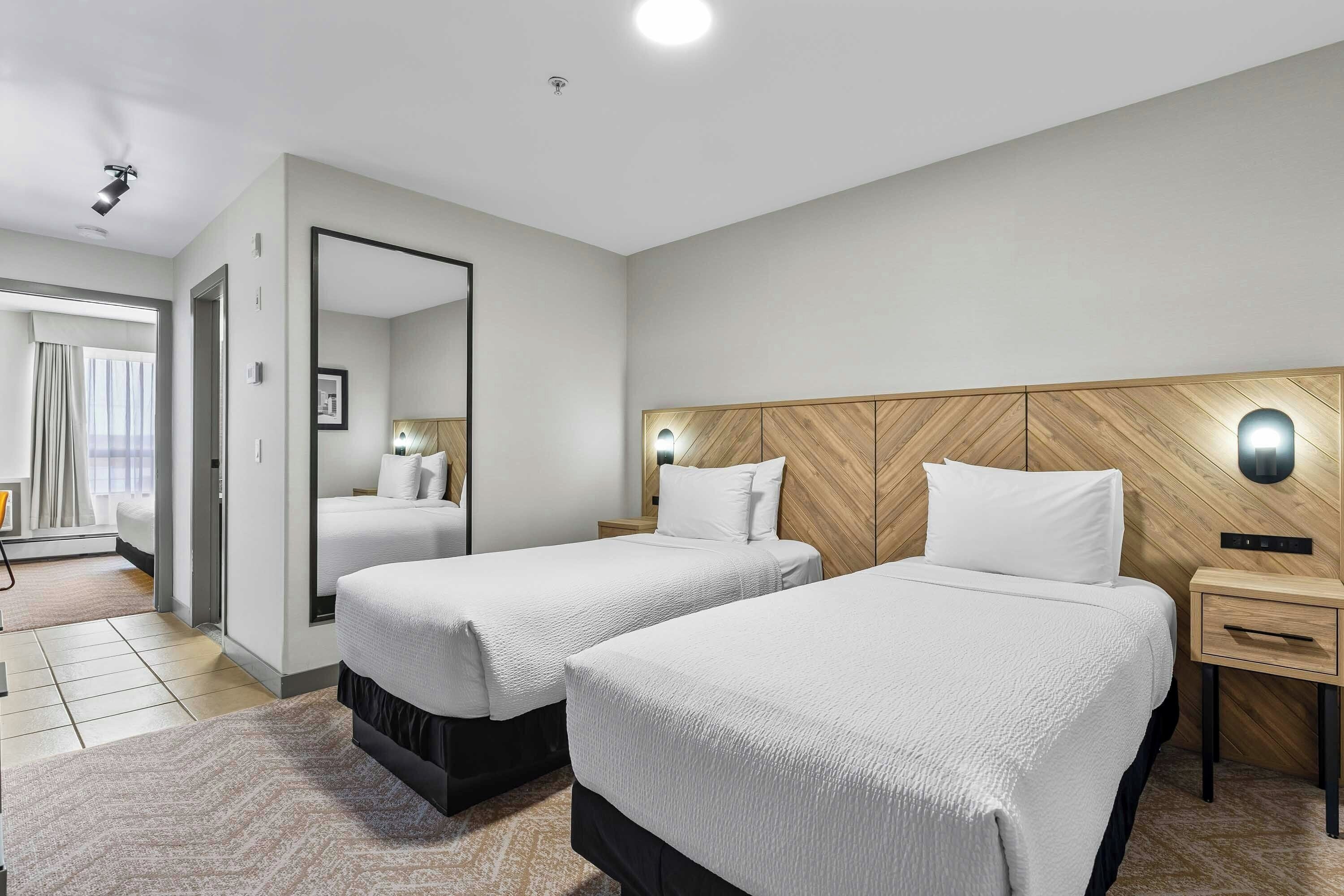 A hotel room with two beds, a wooden headboard, a nightstand, a mirror, and a view of a balcony.