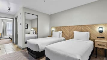 A hotel room with two beds, a wooden headboard, a nightstand, a mirror, and a view of a balcony.