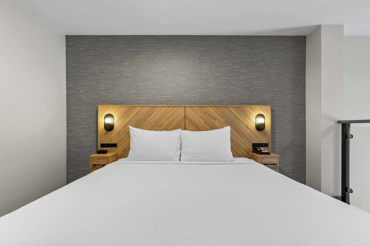 A bed with a wooden headboard and two bedside lamps, a nightstand, and a wardrobe.
