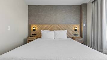 Habitación de hotel con una cama grande, cabecero de madera, dos mesitas de noche y una lámpara fijada a la pared.