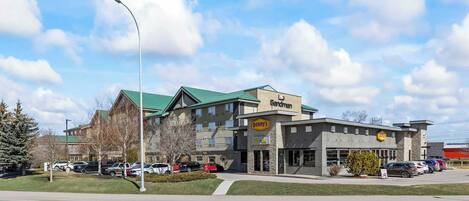 A multi-story building with a green roof, a visible sign for 'Denny's,' and a parking lot with several cars.