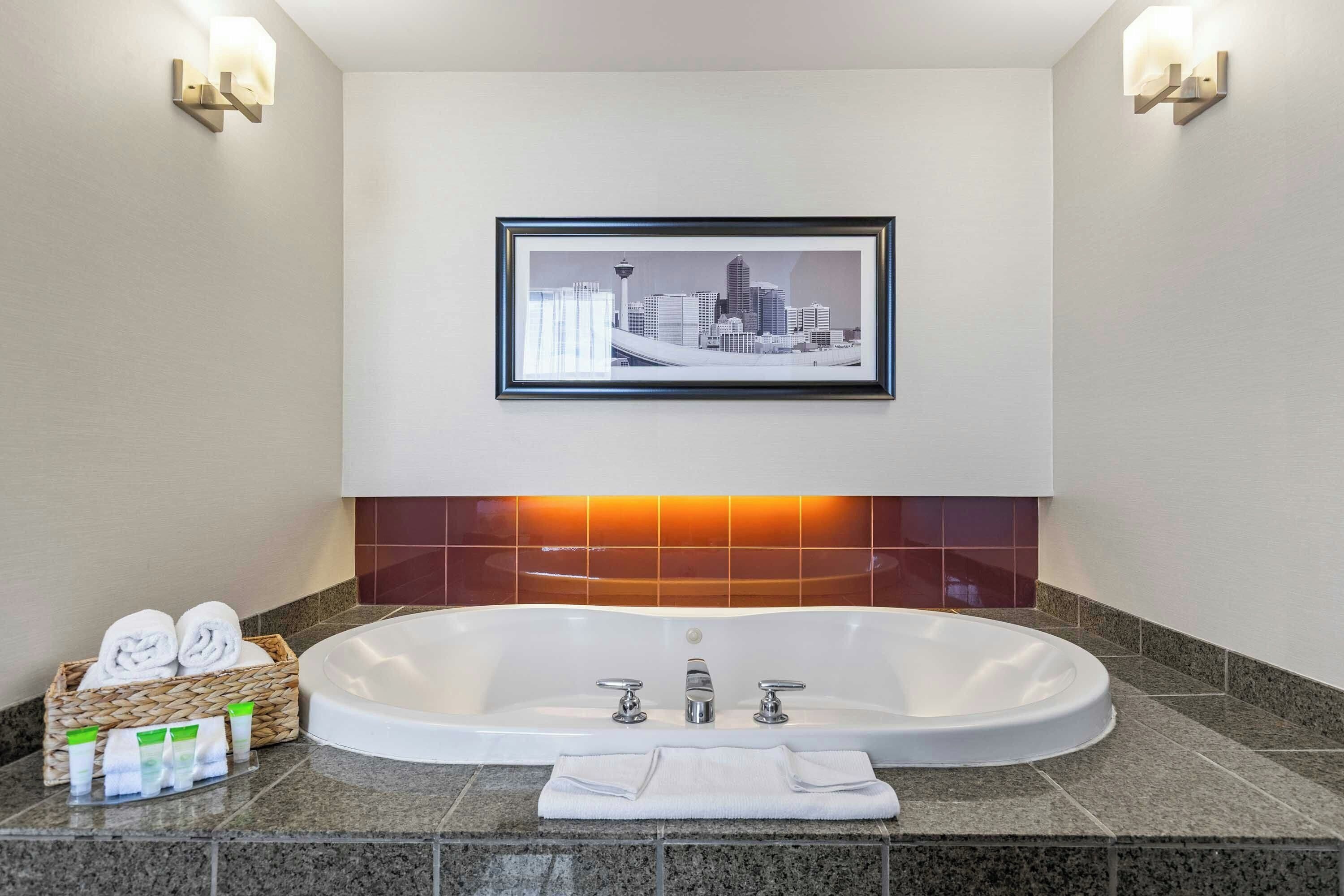 Ein modernes Badezimmer mit einer großen Badewanne, einem Stadtbild in einem Bilderrahmen und zwei Wandleuchten.