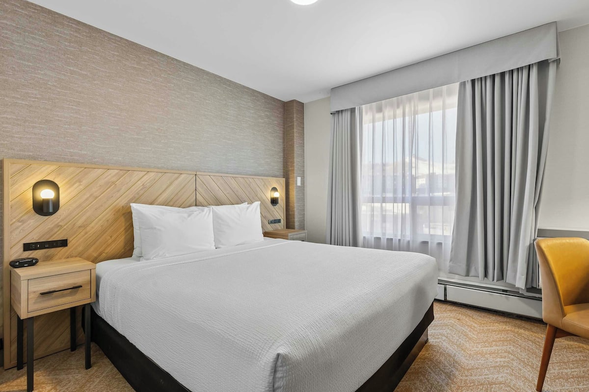 A hotel room with a large bed, a nightstand, a chair, and a window with curtains.