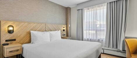 Una habitación de hotel con una cama grande, una mesita de noche, una silla y una ventana con cortinas.