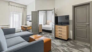 A hotel room with a sofa, ottoman, desk, TV, wardrobe, and a bed. - Sandman Hotels & Suites Calgary West (Calgary)