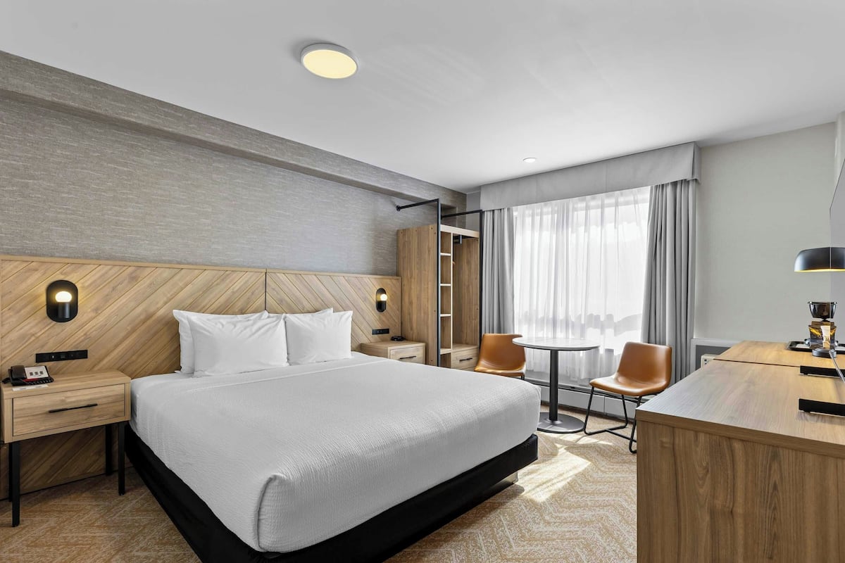 A hotel room with a bed, bedside tables, a desk, chairs, and a window with curtains.