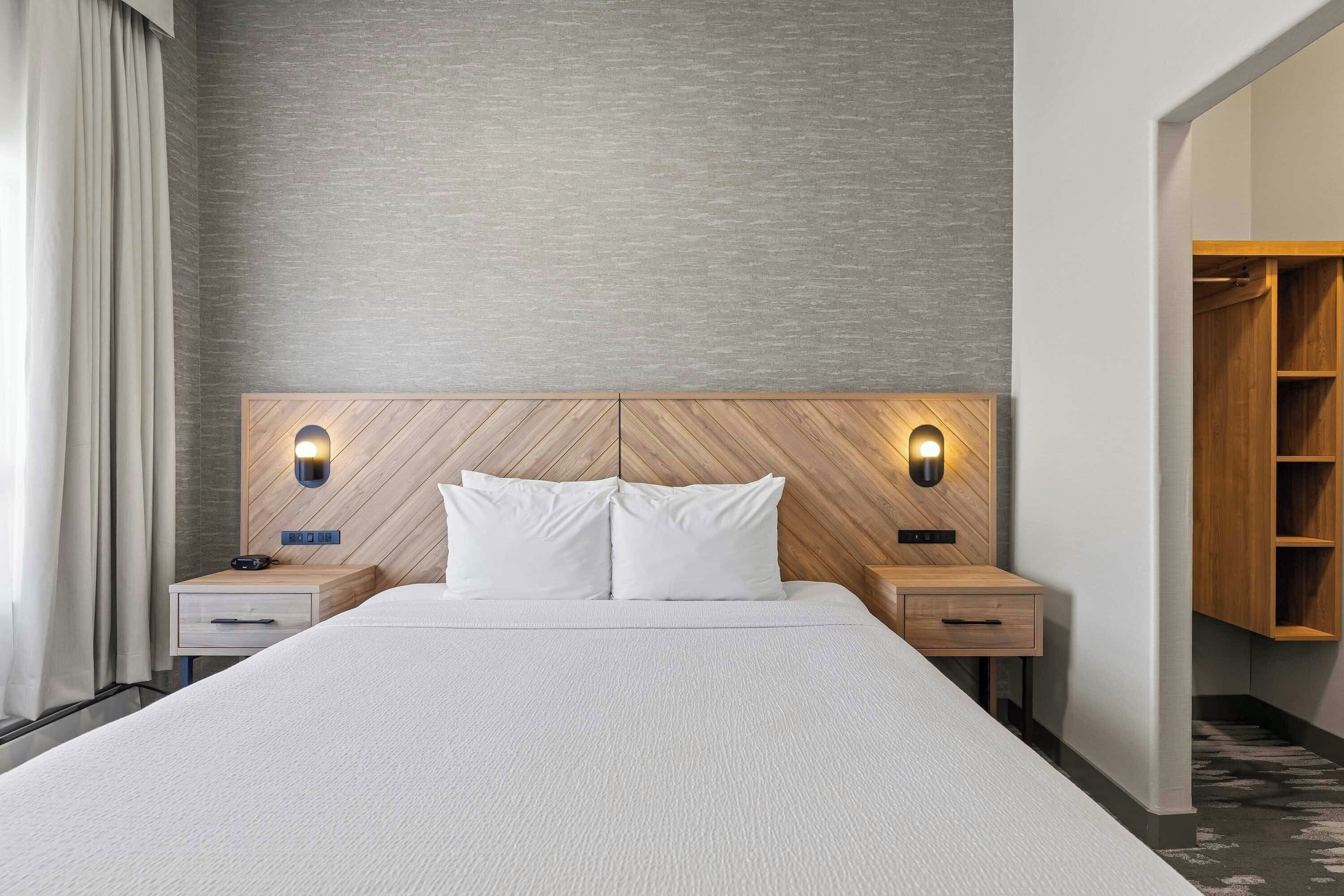 A hotel room with a large bed, wooden headboard, bedside tables with lamps, and a wardrobe.