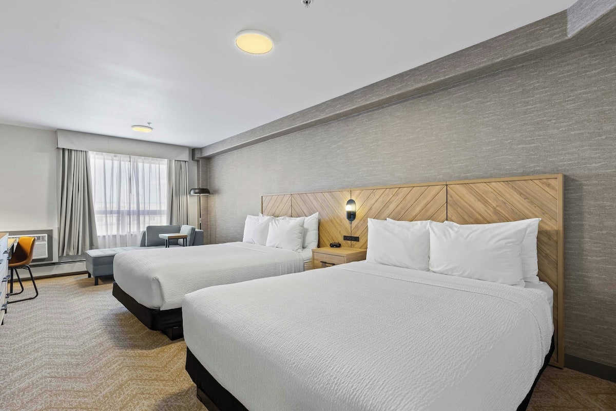 A hotel room with two beds, a desk, a chair, and a window with curtains.