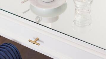 Una mesa de vidrio blanca con una taza y un vaso, un tirador de bronce y una silla azul.