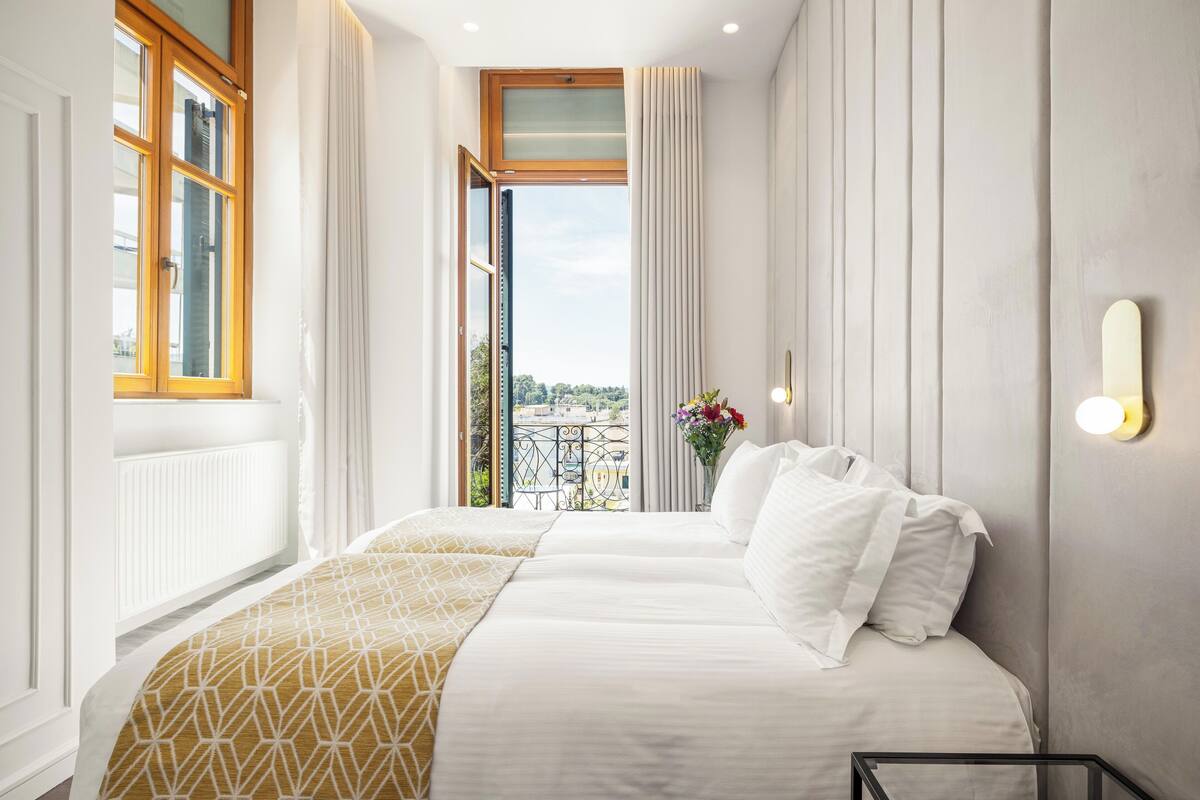 Una habitación de hotel con una cama grande, vistas a la ciudad y un balcón con barandilla.