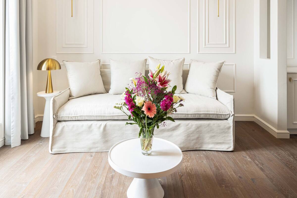 Una sala moderna con un sofá color beige, una mesa de centro redonda blanca y una araña dorada.