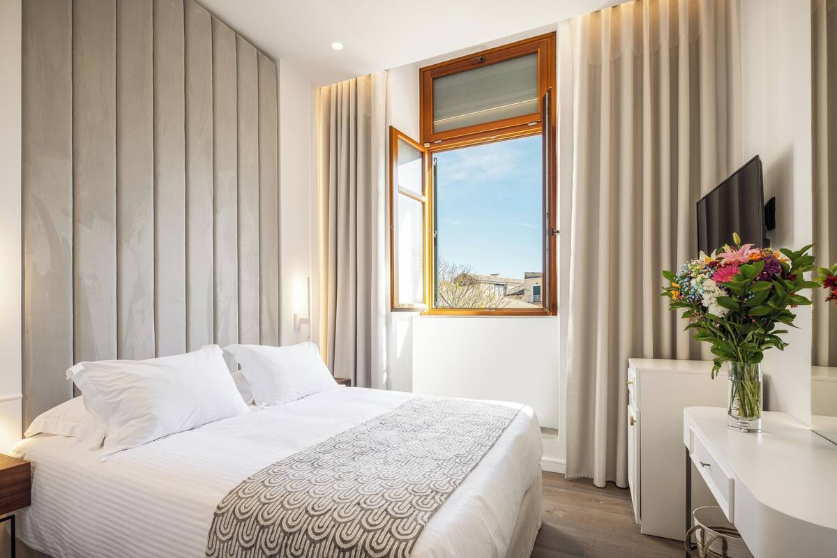 Habitación de hotel con cama, escritorio, televisión y ventana con cortinas.