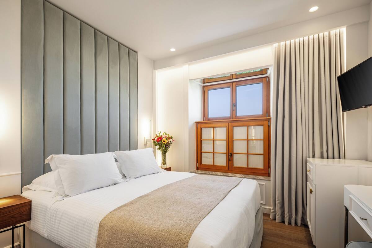 Una habitación de hotel con una cama, un armario de madera, un televisor y una ventana con cortinas.