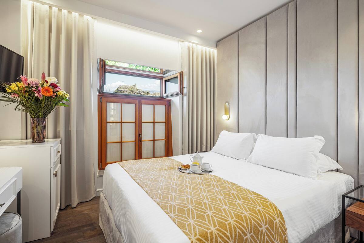 Habitación de hotel con cama, escritorio, un jarrón de flores y ventana con cortinas.