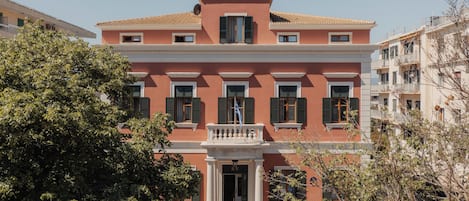 A multi-story building with a central entrance, balconies, and a tiled roof.