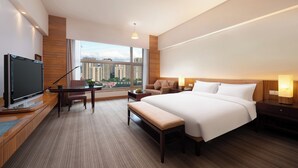 Een moderne hotelkamer met een groot bed, een bureau met stoel, een televisie en uitzicht op de stad door grote ramen.