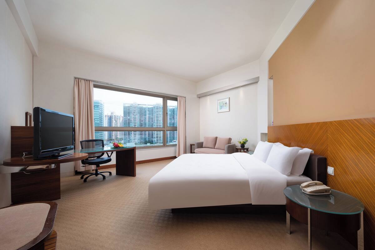 Habitación de hotel con una cama grande, un escritorio con computadora, televisión y ventana con vista a la ciudad.