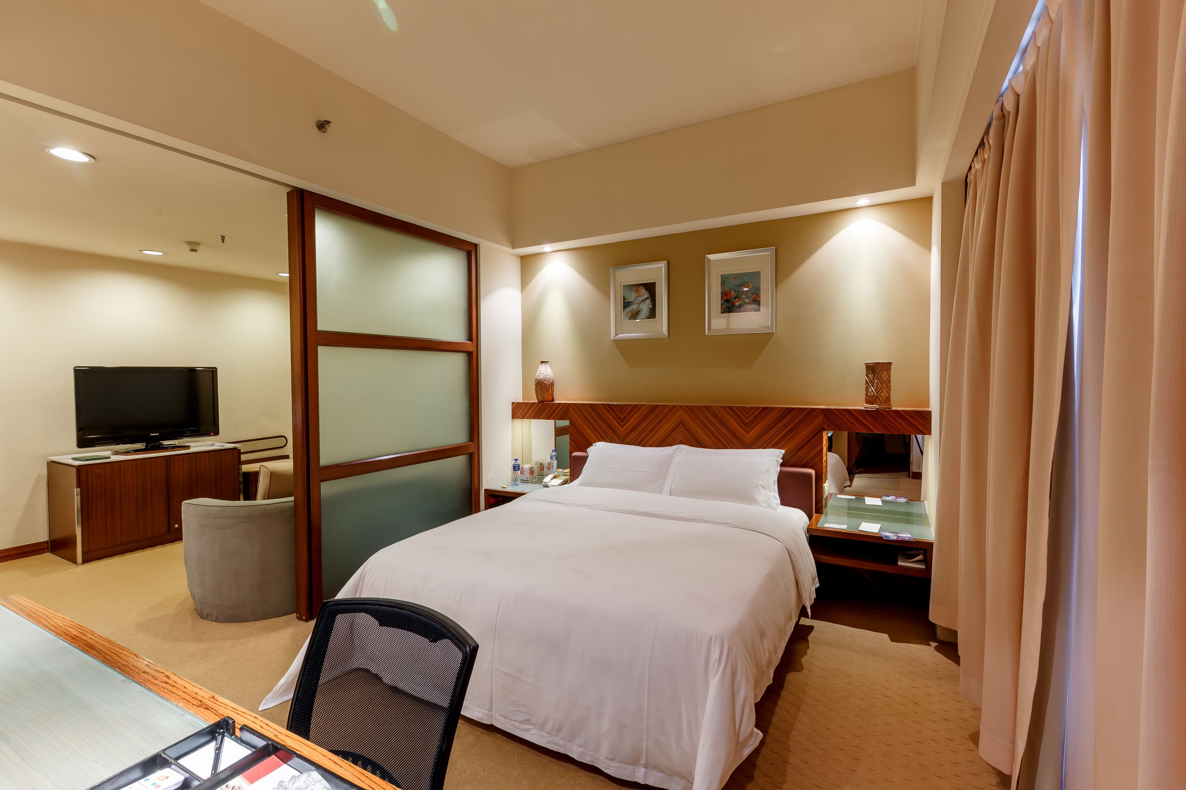 A hotel room with a large bed, a desk with a computer, a television, and a small table with a lamp.