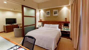 A hotel room with a large bed, a desk with a computer, a television, and a small table with a lamp.